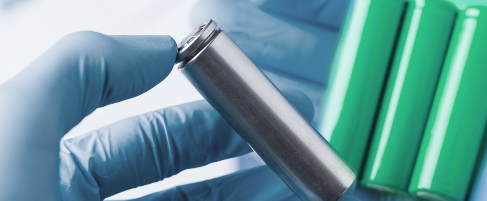Gloved hand holding silver Lithium battery, green Lithium batteries in the back